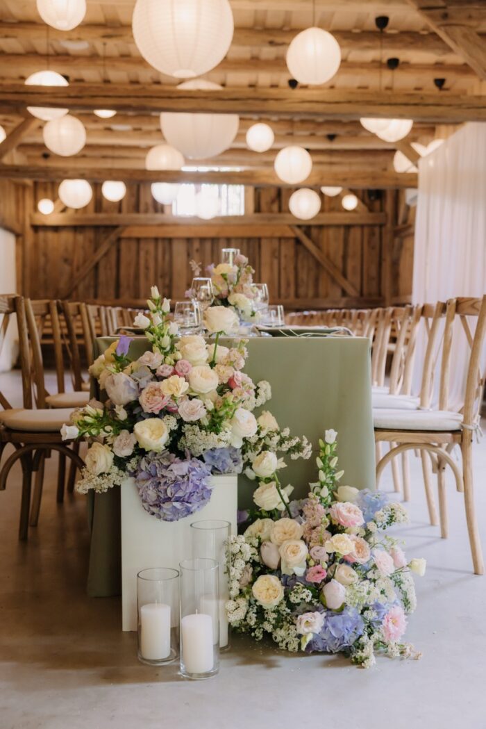 Blumenarrangement in Pastelltönen auf der Hochzeitstafel im Holzstadl