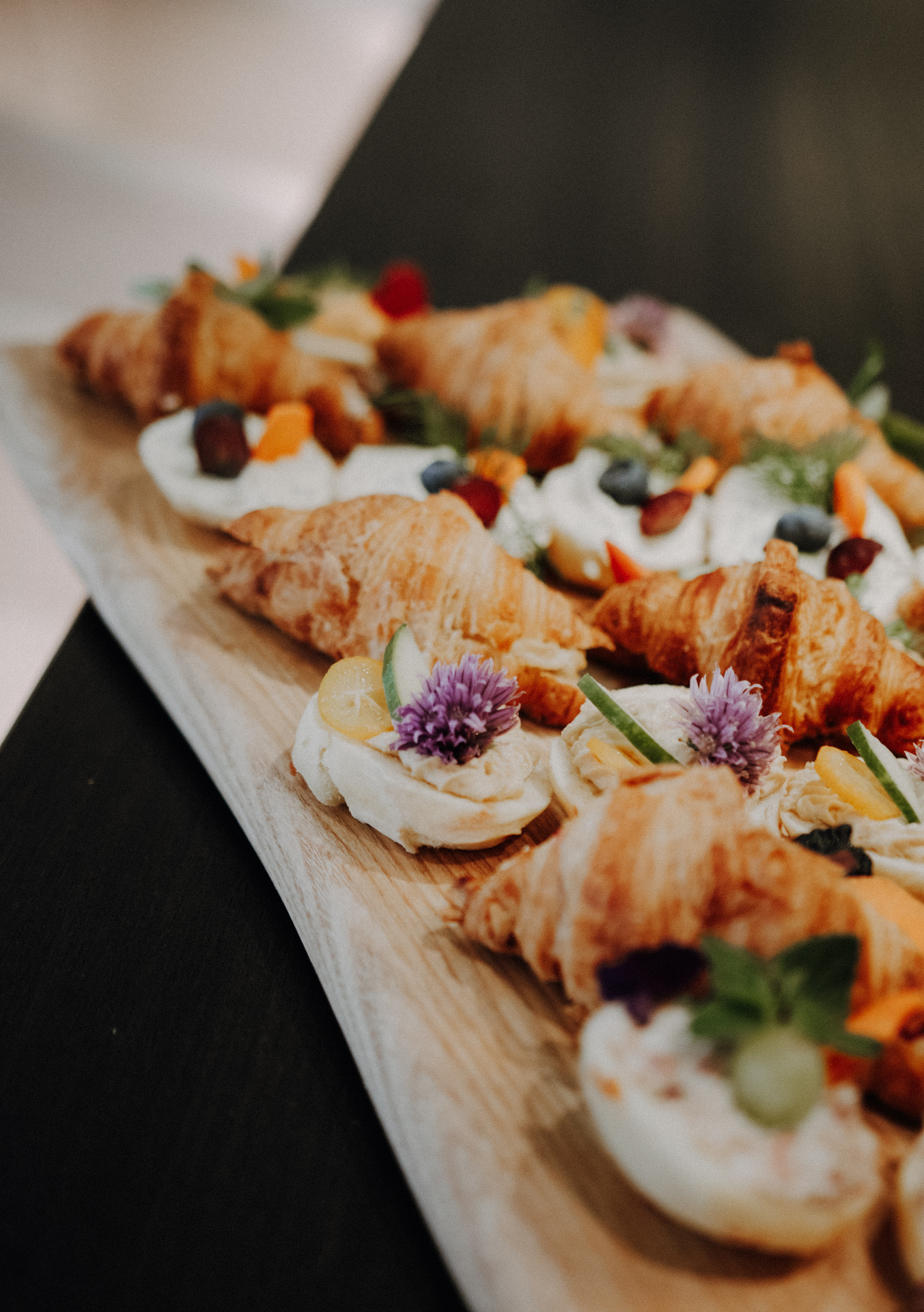 Fingerfood mit Croissants und essbaren Blüten auf einem Holzbrett