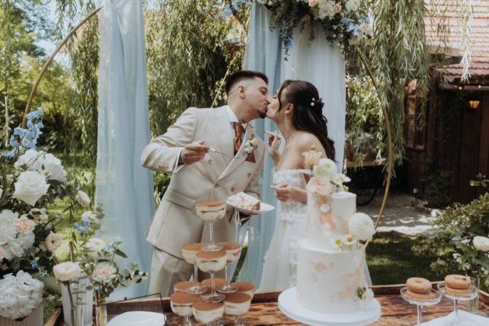 Brautpaar küsst sich beim Anschneiden der Hochzeitstorte im Garten