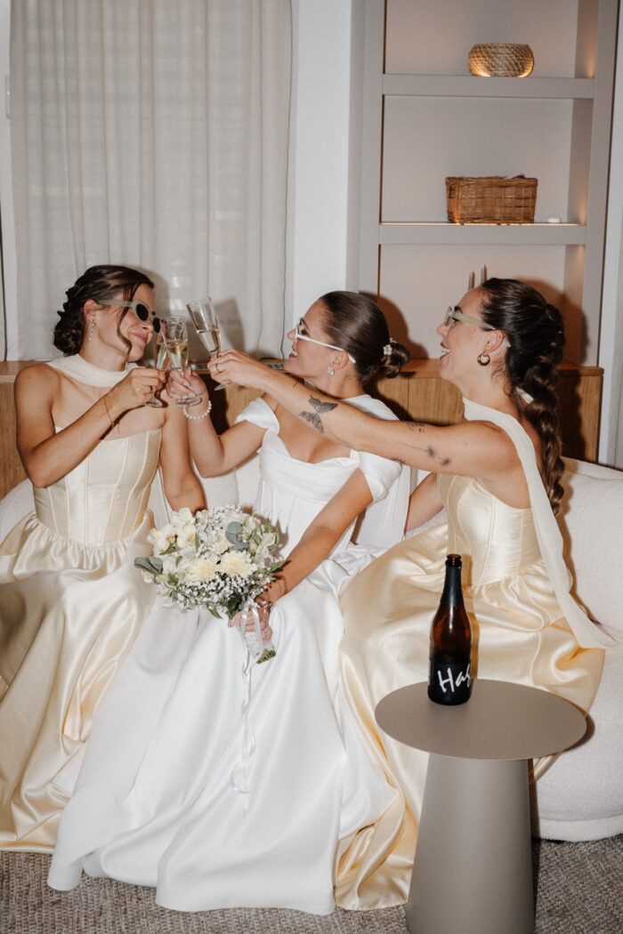 Bridesmaids in Butter Yellow stoßen beim Getting Ready mit der Braut an